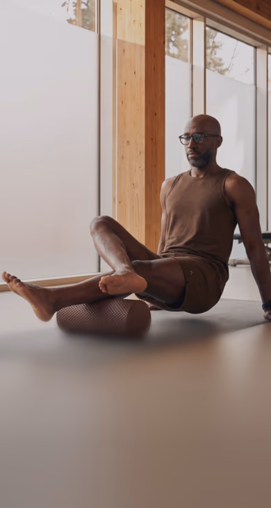 New employee stretching on a yoga mat with a BetterMe foam roller under his legs in a sunlit studio