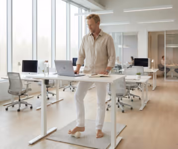 Employee working at a standing desk while rolling a massage ball under his foot in an open-plan office