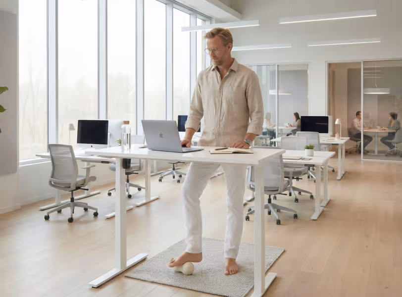 Employee working at a standing desk while rolling a massage ball under his foot in an open-plan office